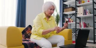 侧视老年妇女在笔记本电脑上进行视频通话，居家在线医疗数字技术服务咨询