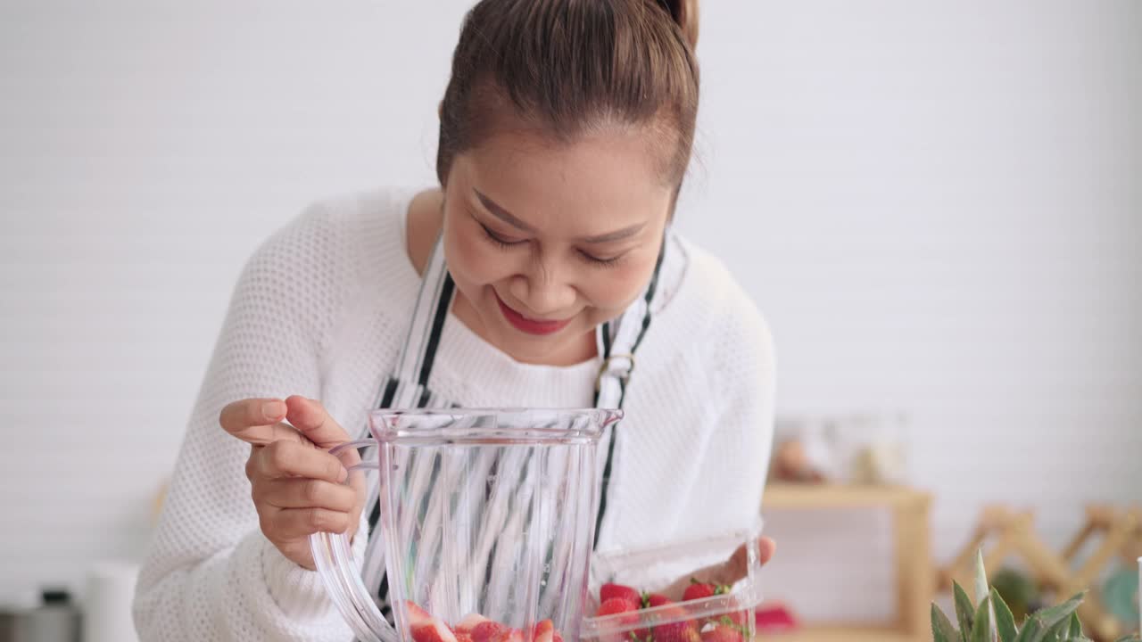 亚洲高级妇女教如何自制水果冰沙与不同的口味，草莓，和酸奶。健康的天然益生菌调味饮料，正面，慢镜头。