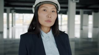 优雅的亚洲商业女士的肖像，戴着防护头盔，站在空厂房内视频素材模板下载