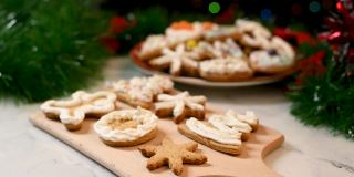 女人用白色奶油糖霜装饰雪花形状的圣诞自制姜饼饼干。厨房桌上放着圣诞糖果。传统的圣诞准备。