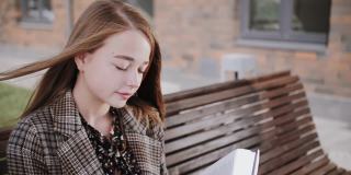 一个金发的年轻女孩在长凳上看书