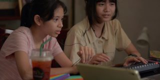 两个可爱的亚洲少女喜欢在家里用电脑键盘和数码设备玩在线视频游戏。年轻玩家与朋友交流互动的直播，