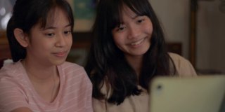两个亚洲可爱女孩喜欢在家里用电子平板电脑和朋友视频聊天。现代年轻人的生活方式。通过数字设备直播的社交网络交流。