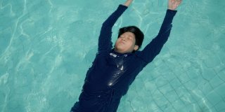快乐的亚洲男孩回到浮在游泳池在度假酒店或度假村与家人，生活理念。