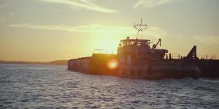 日落背景中一艘驳船的剪影。水路货物运输。美丽的景观象征着货物运输到买家