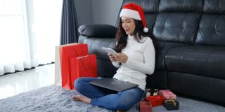 一名戴着圣诞帽的女子在客厅里用电子平板电脑网购圣诞礼物