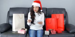 一名戴着圣诞帽的女子在客厅里用电子平板电脑网购圣诞礼物