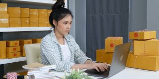 快乐的女人工作与她的笔记本电脑和快递包裹在家里的办公室