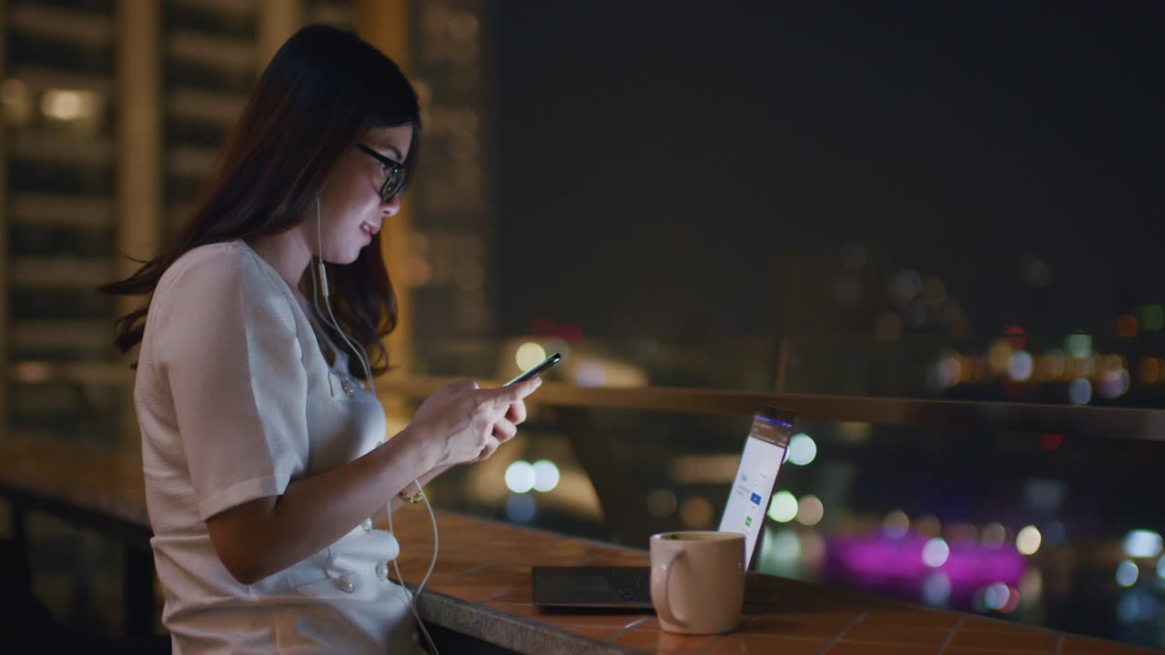 美丽的亚洲女人在晚上用智能手机欣赏音乐