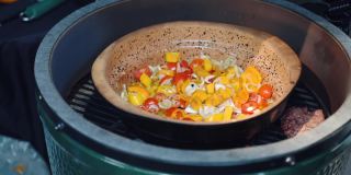 街头小吃烧烤，人们在烧烤架上用钳子搅拌蔬菜汤沸腾。新鲜切碎的洋葱，甜椒和西红柿在碗里煎。健康素食汤，垃圾食品概念
