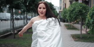 穿着白色毯子的漂亮女孩走在街上。慢动作