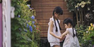 2个亚洲的中国年轻姐妹手牵着手，在周末的晚上在房子的前院跳来跳去，一起开怀大笑