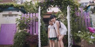 亚洲华人2个小女孩姐妹在晨光中站在充满牵牛花的房子前院看着镜头微笑
