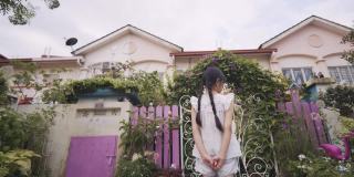 开朗的亚洲华人小女孩在晨光中在布满牵牛花的房子院子里关上大门