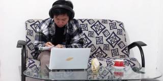 亚洲男性工作在家里使用笔记本电脑视频会议电话会议耳机