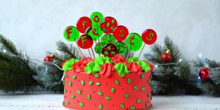 用球装饰圣诞蛋糕，球上写着德语Frohes Fest节日快乐。一个女人的手插在蛋糕上的装饰。