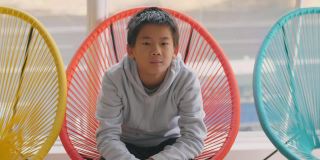 快乐和自信的混血儿亚洲男孩微笑和坐在彩色的红色椅子，青少年肖像