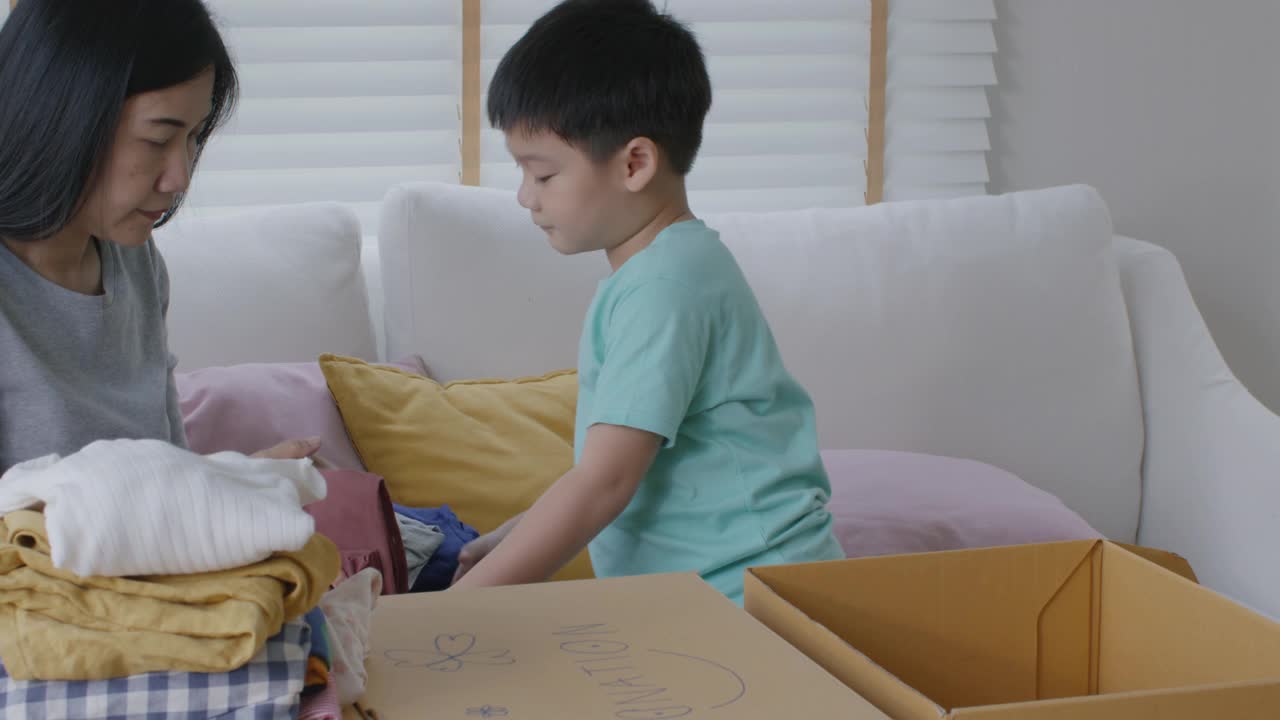 亚洲妈妈和孩子准备在家里捐赠旧衣服包装盒。