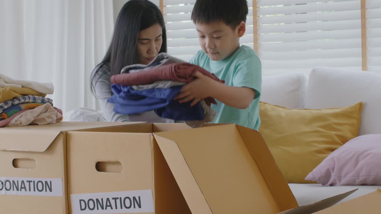 亚洲妈妈和孩子准备在家里捐赠旧衣服包装盒。