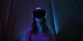 年轻漂亮的女孩使用虚拟现实眼镜。坐在霓虹灯下的黑暗房间里，戴着VR头盔玩游戏