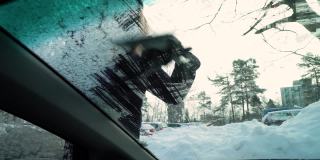 年轻女子用雪刷刮掉汽车挡风玻璃上的冰