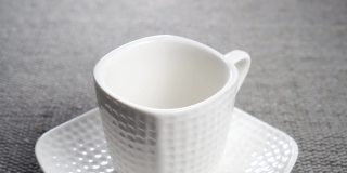 把一个茶包浸入一个白色的空茶杯里，茶托放在一个灰色的有纹理的灰色垫子上