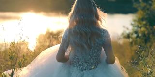 美丽的新娘跑向夕阳下的湖。Moranrange的日落和光线在背光上。穿着雪纺长裙的年轻女子