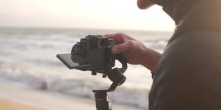电影制作人在日出时用电子稳定器在海滩上用相机拍摄视频