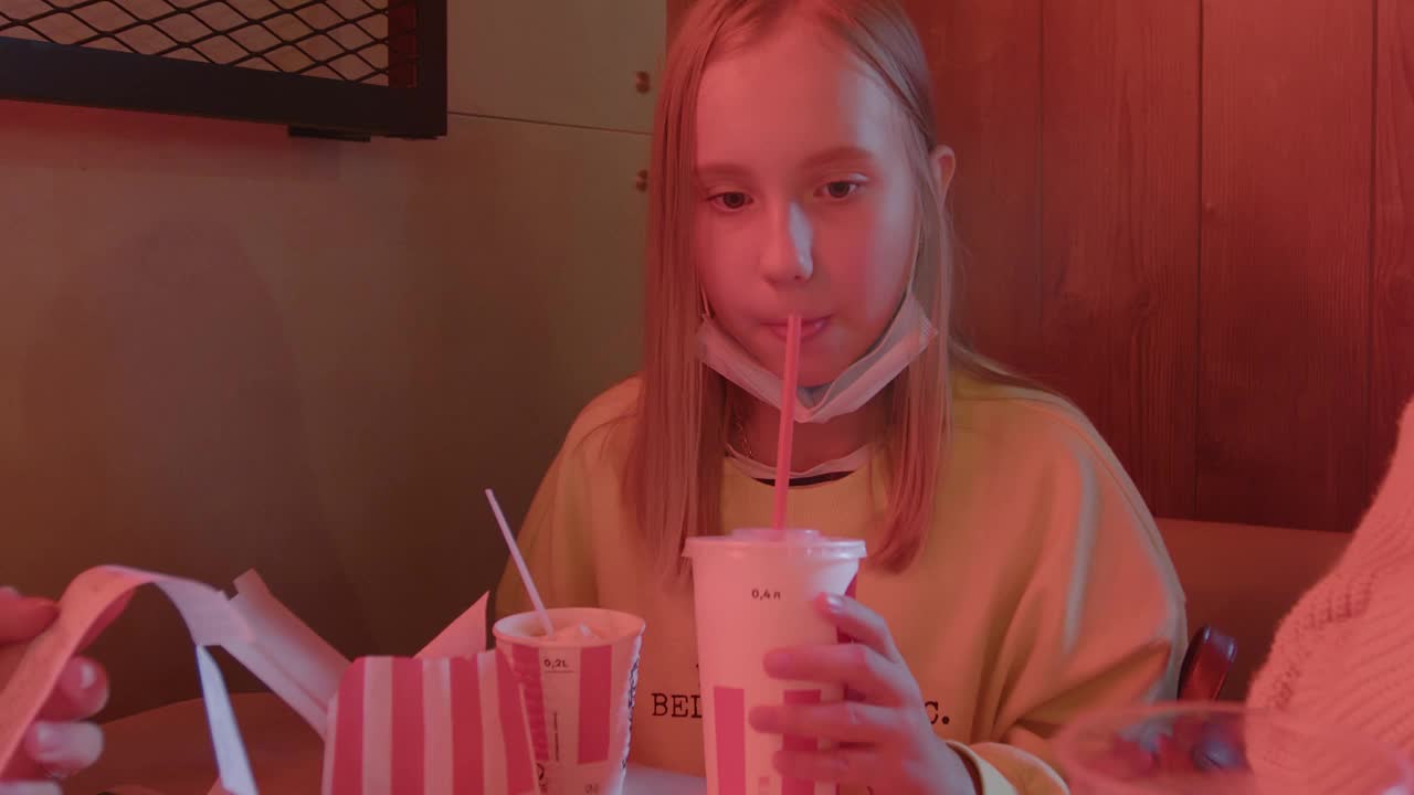 一个十几岁的女孩在咖啡馆吃鸡肉和喝苏打水。