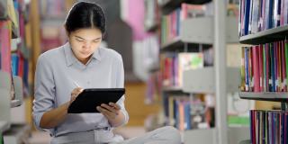 亚洲大学图书馆，一名亚洲女子正在图书馆用平板电脑上网。