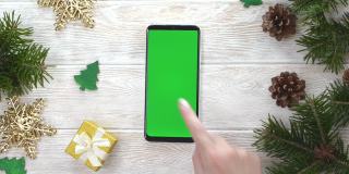 绿屏技术手机在圣诞装饰桌上俯视图平放，模拟空间文字复制，手人使用智能手机色度键，新年在线概念