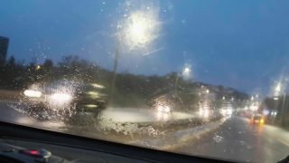 特写大雨落在汽车的挡风玻璃上，雨刷工作迅速。雨点从汽车前窗倾泻而下。开着前灯的汽车在高速公路上开会。4 k的片段视频素材模板下载