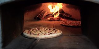在露天的柴火烤箱中烘烤传统披萨。面包师的手把生披萨放进砖烤炉里。意大利披萨