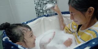快乐的亚洲孩子们在塑料浴缸里对着姐姐的脸吹泡泡，生活理念。