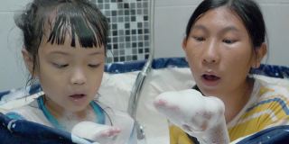 快乐的亚洲孩子们在塑料浴缸里一起吹泡泡，生活理念。