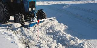 慢动作视频。在晴朗的霜天里，一辆拖拉机用铲子把雪堆成一堆