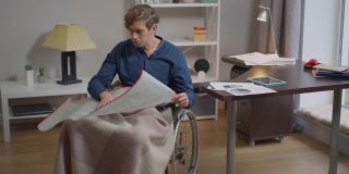 集中的智能残疾自由职业者建筑师的肖像分析与笔在慢动作的蓝图写作。体贴的白人男子坐在轮椅上在家工作。住相机。