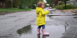 一个滑稽可爱的小女孩，穿着黄色防水外套和靴子在雨中玩耍