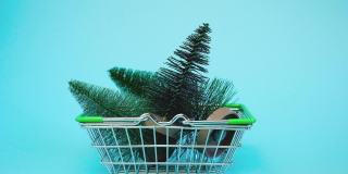 把小圣诞树放进购物车的手。蓝色背景下超市手推车上的人造迷你圣诞树。圣诞节，新年，假日购物概念。极简主义。