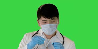 年轻的亚洲医生正在从安瓿溶液与一个注射器上的绿色屏幕，Chroma关键
