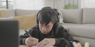 亚洲十多岁的男孩在家用笔记本电脑视频通话，使用zoom在线虚拟课堂，孩子们在家上学，新冠疫情期间远程学习，新常态概念
