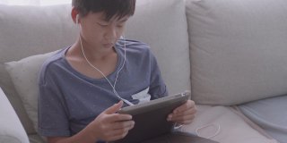 亚洲混血儿十几岁的男孩在家里用数字平板电脑进行视频通话，使用zoom在线虚拟课堂，社交距离，家庭教育，远程学习，新常态概念