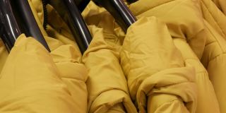 温暖的黄色冬季夹克挂在女装精品店的衣架上