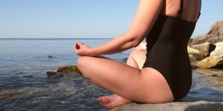 日出时分，一位身着黑色泳装的年轻女子在海边的沙滩上练习瑜伽、健身和普拉提。健康的生活方式。在户外的大自然中放松身心。和谐冥想观