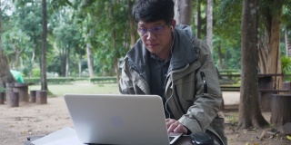 亚洲男人用森林背景的笔记本电脑工作。男性除了在家和办公室外，还会在旅行时在线工作。