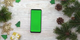 绿屏技术手机在圣诞装饰桌上俯视图平放，模拟空间文字复制，手人使用智能手机色度键，新年在线概念