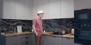 一个戴着帽子的年轻人一边做饭一边在厨房里唱歌跳舞