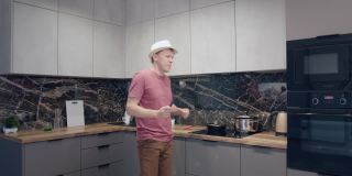 一个戴着帽子的年轻人在厨房边做饭边拿着勺子边唱歌边跳舞