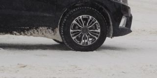 汽车正站在冬天城市里白雪覆盖的十字路口。降雪。车轮的慢动作特写。轮胎面。交通状况不佳，暴风雪。危险之旅