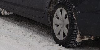 汽车正行驶在冬季城市里积雪覆盖的道路上。排气管中冒出的烟雾。降雪。车轮的慢动作特写。轮胎面。交通状况不佳，暴风雪